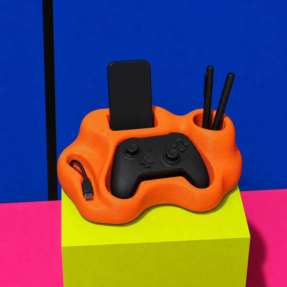 Concept render of an orange 3D-printed blob-shaped desk dock holding a phone, controller, cable, and pens.